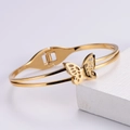 Detailed view of an open golden butterfly bangle on a white textured display block - Gold