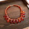 Detail view of amber resin beads and gold metal links on a dark wood tray - Amber Oval Style