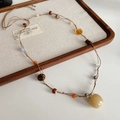 Détail d'un pendentif pomme en œil de tigre sur un collier tressé à la main avec perles - Collier-Café