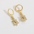 Detail of golden turtle earrings with green zircons and evil eye pattern in center - Black Turtle