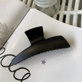 Close-up of a large matte black hair claw clip resting on a white book with soft lighting - Matte Black