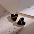 Detailed close-up of heart-shaped black earrings with gold chain link on stone background - Black