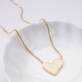 Golden heart necklace with marble inlay and sleek snake chain on a ceramic plate - White