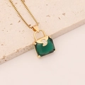 Detailaufnahme der goldenen Kette mit grünem Edelstein-Handtaschenanhänger auf Stein - Dunkelgrün