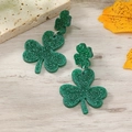 Close-up of green glitter clover earrings with horseshoe detail on a wooden surface - Simple Shamrock Style (WEH4137)
