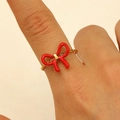 Fashionable gold stainless steel ring with a vibrant red enamel bow on a finger - Bright Red Enamel Bow Style (DZ-547)