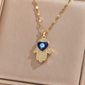 Detailed view of a gold Hamsa Hand pendant with a heart-shaped blue Evil Eye and crystals - Gold White Zircon Blue Oil
