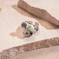 Primer plano de anillo plateado con cuentas coloridas sobre fondo de piedra beige - Textura de Lava Irregular (HR2616) / Flor Azul