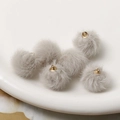 Macro shot of grey faux rabbit fur pompom charms with golden metal loops for DIY jewelry - Gray