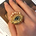 Artistic gold evil eye ring with green center and pearls on a vintage book background - Ring