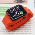Digital sports watch with vibrant orange silicone strap on an open book background - Orange