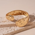 Detailweergave van een brede gouden armband met gehamerde textuur op een beige steen - Gehamerde Textuur Open Armband / Goud