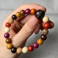 Detailed view of colorful multi-wood prayer beads held by hand showing texture and size - Old Style