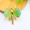 Elegant gold butterfly brooch featuring green heart-shaped crystal wings on a wood coaster - Gold Plated Green Aventurine