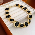 Detalle de un collar dorado con cristales negros en un lujoso estuche de joyería de terciopelo - Collar / Dorado