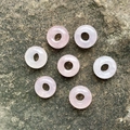 Set of seven natural pink quartz donut beads arranged on a textured rock surface - Rose Quartz