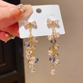 Dettaglio di orecchini etnici con fiocco dorato e perle di cristallo in mano - 3# Perno per orecchini in argento - Fiocco dorato Orecchini a nappa blu-viola
