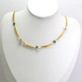 Detailed close-up of golden chain necklace with multiple blue evil eye beads on white display - Blue