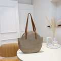 Borsa tote estiva in paglia intrecciata con spalline in pelle su un tavolo bianco - Marrone