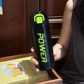 Close-up of matte black sports bottle with neon green lock held by a hand in lifestyle setting - Black