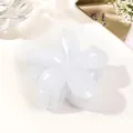 Detailed close-up of a glossy white flower hair claw clip on elegant fabric and magazine - Jelly Milk White