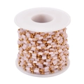 Macro view of gold stainless steel chain with pink stone beads on a white spool - Gold-Pink
