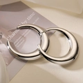 Close-up of chunky silver-plated crescent hoop earrings on a warm cream background - Silver