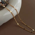 Detail of layered gold titanium steel necklace with flat round discs on ceramic - Gold Flattened Chain