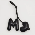 Close-up of black leather M-letter and heart charm with refined hand-stitched detailing - Black Heart and Black M