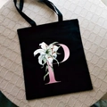 Black canvas tote bag with pink letter P and lily flower print on woven surface - Letter P / Black