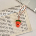 Dettaglio di un ciondolo a fragola in peluche con ricamo su un libro aperto - Carota