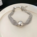 Detail of silver multi-layered chain bracelet with a central metal bead on a white plate - Necklace - Silver