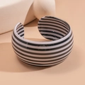 Detailweergave van brede acryl armband met zwart-witte strepen op beige achtergrond - Zwart Wit Horizontale Strepen