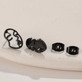 Close-up of black minimalist abstract face earrings on a textured ceramic dish - Black