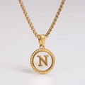 Macro shot of gold necklace with a round shell pendant featuring a raised letter N detail - Letter N