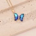 Collier papillon doré avec pendentif en cristal dégradé bleu sur une surface en pierre beige - Bleu clair