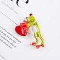 Graziosa spilla a rana smaltata verde con cuore rosso e bordi dorati su carta - Rana con Cuore