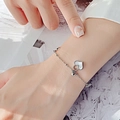 Silver steel bracelet featuring heart shell pendant and small bell on female wrist - Silver