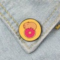 Cute cartoon capybara on a pink donut enamel pin displayed on blue denim fabric - Pink Donut Capybara