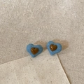 Dettaglio di orecchini a cuore in denim con centro in resina su sfondo di lino beige testurizzato - Cuore Marrone - Denim Blu