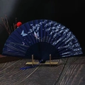 Close-up of dark blue folding fan with silver floral patterns and blue tassel on stand - Blue Fallen Cherry Blossoms