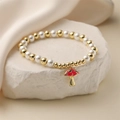 Armband mit goldenen Perlen und rotem Pilzanhänger auf weißem Steinuntergrund - Barbie-Rosa