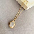 Gros plan détaillé d'un collier rétro doré avec pendentif opale blanche et métal gravé - Collier en Acier Titane Pierre Ovale Blanc Laiteux
