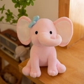 Soft pink plush elephant toy with blue bow tie on a cozy wooden background - Pink With White Ear Core/Blue Bow