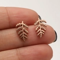 Detail of rose gold leaf earrings featuring hollow metal texture held between fingers - Leaf / Rose Gold