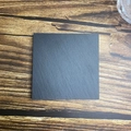 Top-down view of a square black natural slate coaster on a brown wood background - Straight Edge Square Style