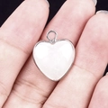 White heart-shaped resin pendant with silver metal bezel held by fingers - White Jade Silver Edging