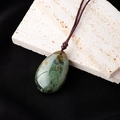 Green water drop natural stone pendant with brown braided cord on a white stone base - Moss Agate Teardrop Pendant