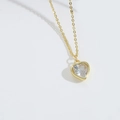 Close-up of golden necklace with a heart-shaped clear zircon pendant in natural light - White