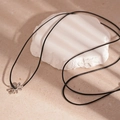 Collar minimalista con colgante de margarita plateada y cordón negro sobre fondo de piedra - Collar Estilo Margarita